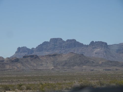 A rugged mountain range rises against a clear blue sky, surrounded by arid desert landscape.