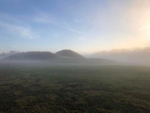 A misty landscape with rolling hills under a soft blue sky, creating a serene and tranquil atmosphere.