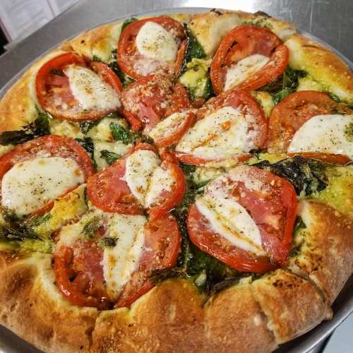 A freshly baked pizza topped with sliced tomatoes, mozzarella, and spinach on a golden crust.