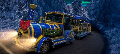 A brightly lit, festive train with a bow, traveling through a snowy mountain landscape under a colorful sky.