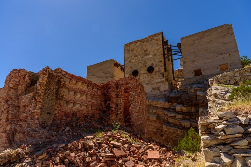 Ruins of an old stone building with crumbling walls and debris under a clear blue sky.