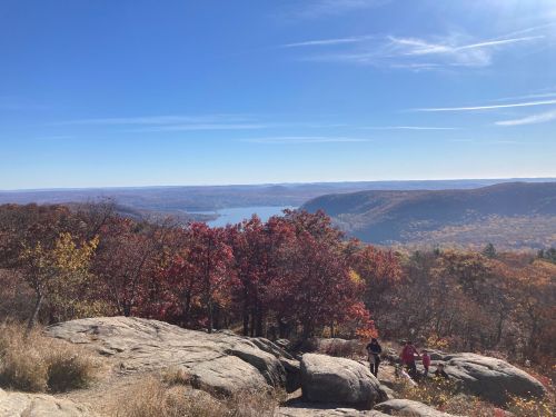 A scenic view from a rocky overlook, showcasing vibrant autumn foliage and a lake in the distance under a clear blue sky.