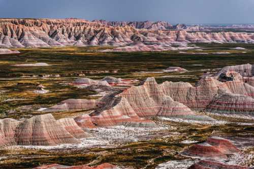 Vast landscape of colorful, layered rock formations and rolling hills under a cloudy sky.