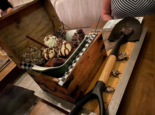 A wooden treasure chest filled with assorted ice cream treats, served with a shovel on a sandy platter.