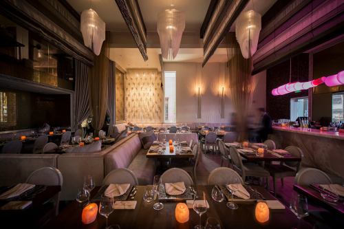 Elegant restaurant interior with soft lighting, modern decor, and tables set for dining. Warm ambiance with candles.