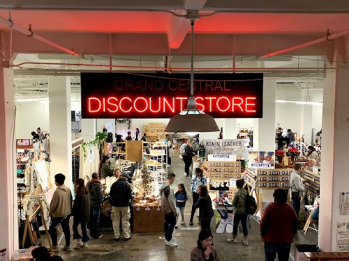 A bustling discount store with a neon sign, featuring various stalls and shoppers exploring the vibrant marketplace.