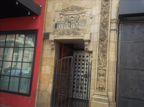 Entrance of Beetle House, featuring ornate stonework and a gated door, set against a red wall.