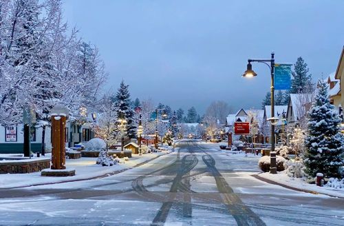 A snowy street lined with trees and cozy houses, illuminated by streetlights in a winter wonderland setting.