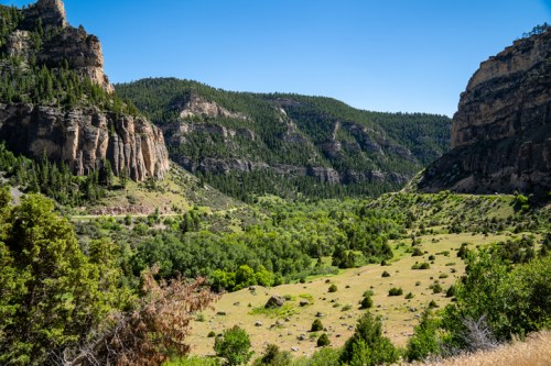 A scenic view of a lush green valley surrounded by rocky cliffs and mountains under a clear blue sky.