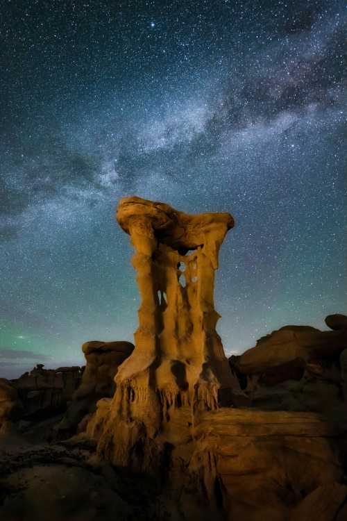 A towering rock formation under a starry sky, with the Milky Way visible in the background.