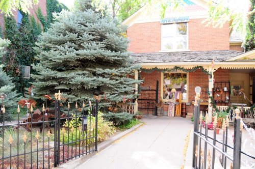 A charming brick building with a garden, surrounded by greenery and a decorative fence.