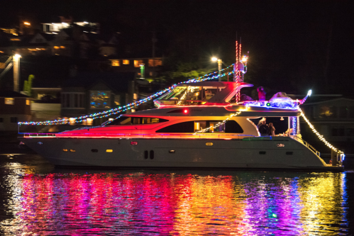 A brightly lit yacht decorated with colorful lights, reflecting on the water at night.