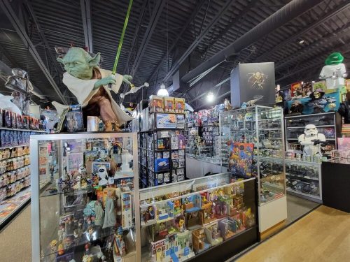 A vibrant toy store filled with collectibles, featuring a large Yoda figure and shelves of various action figures and memorabilia.