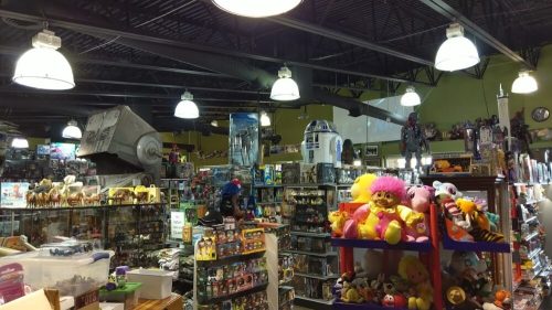 A vibrant toy store filled with shelves of action figures, plush toys, and collectibles under bright overhead lights.