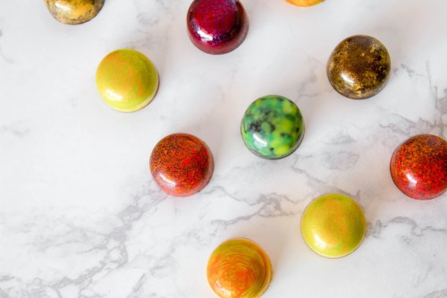 Colorful, glossy chocolate bonbons arranged on a marble surface, showcasing various vibrant patterns and hues.