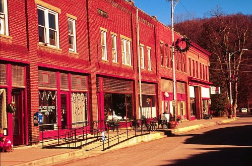 A quaint brick storefronts line a quiet street, decorated for the holidays with festive lights and greenery.