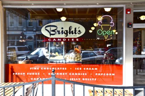 A storefront window of Bright's Candies, featuring a neon "Open" sign and displays of various sweets and treats.