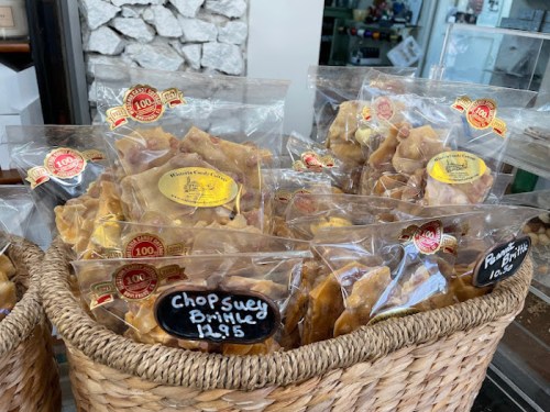 A woven basket filled with clear bags of various snacks, labeled with prices, displayed in a shop.