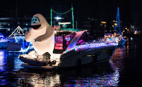 A decorated boat with colorful lights and a large inflatable yeti figure on the water at night.