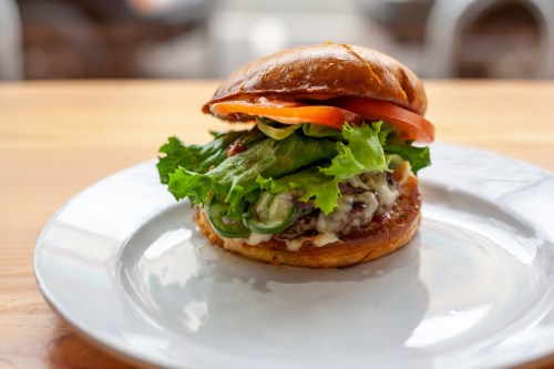 A delicious burger on a plate, featuring a toasted bun, lettuce, tomato, and a juicy patty with sauce.