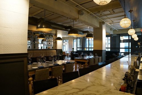 A modern restaurant interior featuring elegant lighting, a marble bar, and neatly set dining tables.