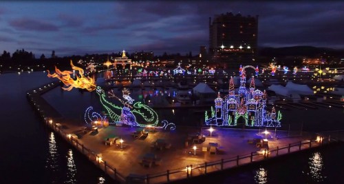 Colorful illuminated decorations of a dragon and castle by a waterfront, with a darkening sky in the background.