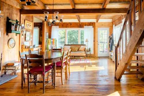 Cozy wooden interior of a cabin with a dining table, chairs, and large windows letting in natural light.