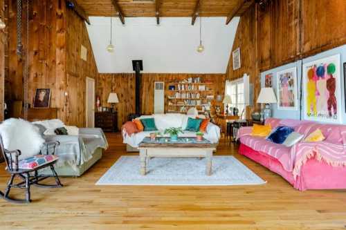 Cozy living room with wooden walls, two sofas, a coffee table, and bookshelves, featuring warm lighting and colorful decor.