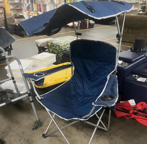 A blue folding chair with a cup holder, surrounded by other furniture in a store.