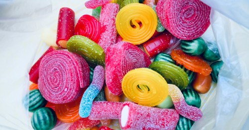 Close-up of a clear plastic bag filled with assorted bulk sour candies, including red fruit rolls and yellow pinwheels.