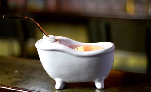 A small white ceramic bathtub filled with a colorful drink and a straw, placed on a wooden surface.