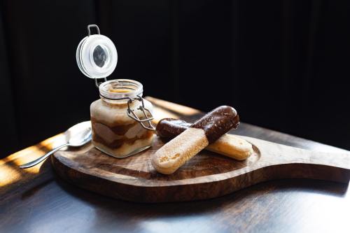 A jar of layered dessert next to two chocolate-covered sponge cakes on a wooden serving board.