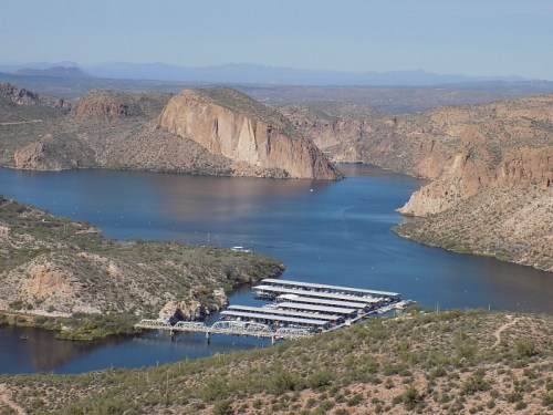 A scenic view of a lake surrounded by rocky hills and mountains, with a marina visible in the foreground.
