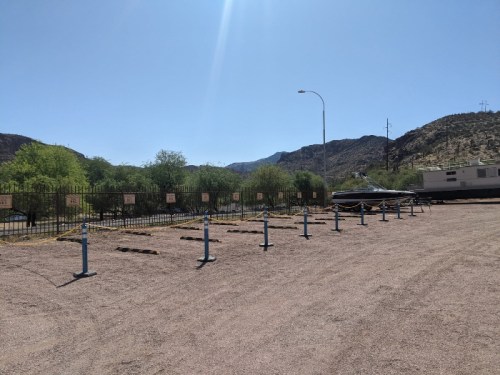 A gravel area with marked spaces, surrounded by fencing and vegetation, under a clear blue sky.