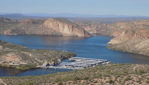 A scenic view of a lake surrounded by rocky hills and mountains, with a marina in the foreground.