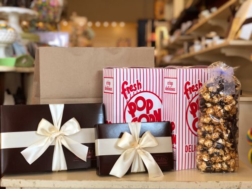A display of popcorn boxes, gift boxes with ribbons, and a jar of caramel popcorn on a table.
