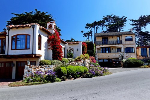 Two charming houses with colorful flowers and greenery, set against a clear blue sky.