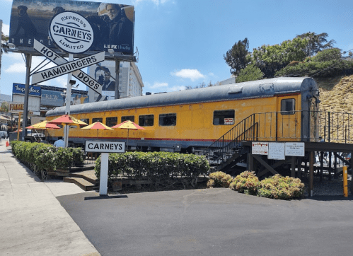 A vintage yellow train car converted into a restaurant, with outdoor seating and a sign reading "CARNEY'S."