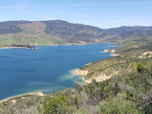A scenic view of a blue lake surrounded by green hills and mountains under a clear blue sky.