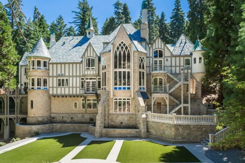 A large, elegant stone mansion with gothic architecture, surrounded by trees and featuring a manicured lawn.