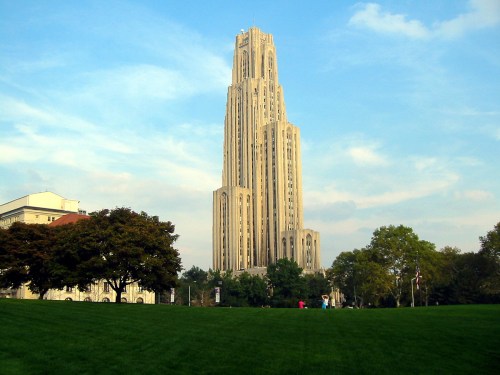 A tall, ornate building rises against a blue sky, surrounded by green grass and trees.