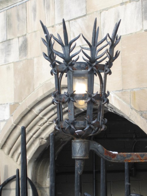 A decorative wrought iron lamp with spiky designs, mounted on a stone wall near an archway.