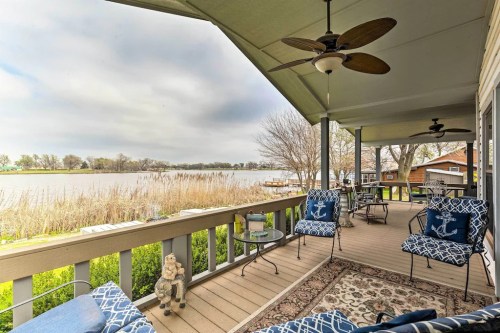 A cozy porch with blue chairs overlooks a calm lake, surrounded by greenery and a cloudy sky.