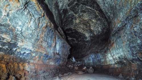 A dark cave interior with textured rock walls and a sandy floor, illuminated by soft light.