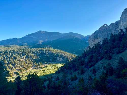 A scenic view of mountains and a valley, with sunlight illuminating the landscape and a clear blue sky above.