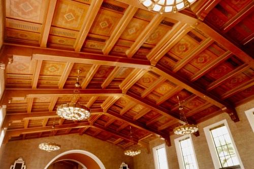 Intricate wooden ceiling with decorative beams and vintage chandeliers in a spacious interior.