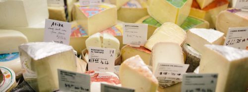 A variety of cheeses displayed with price tags in a market setting.