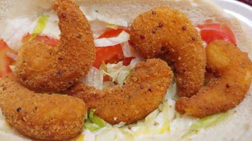 A close-up of a sandwich filled with crispy fried shrimp, lettuce, and tomato on soft bread.