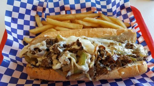 A loaded cheesesteak sandwich with sautéed peppers and onions, served with a side of golden French fries.