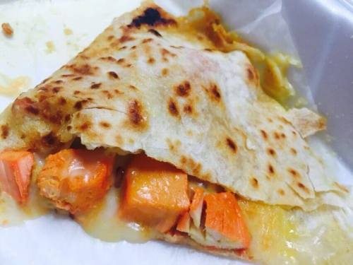 A close-up of a folded tortilla filled with melted cheese and chunks of orange salmon.
